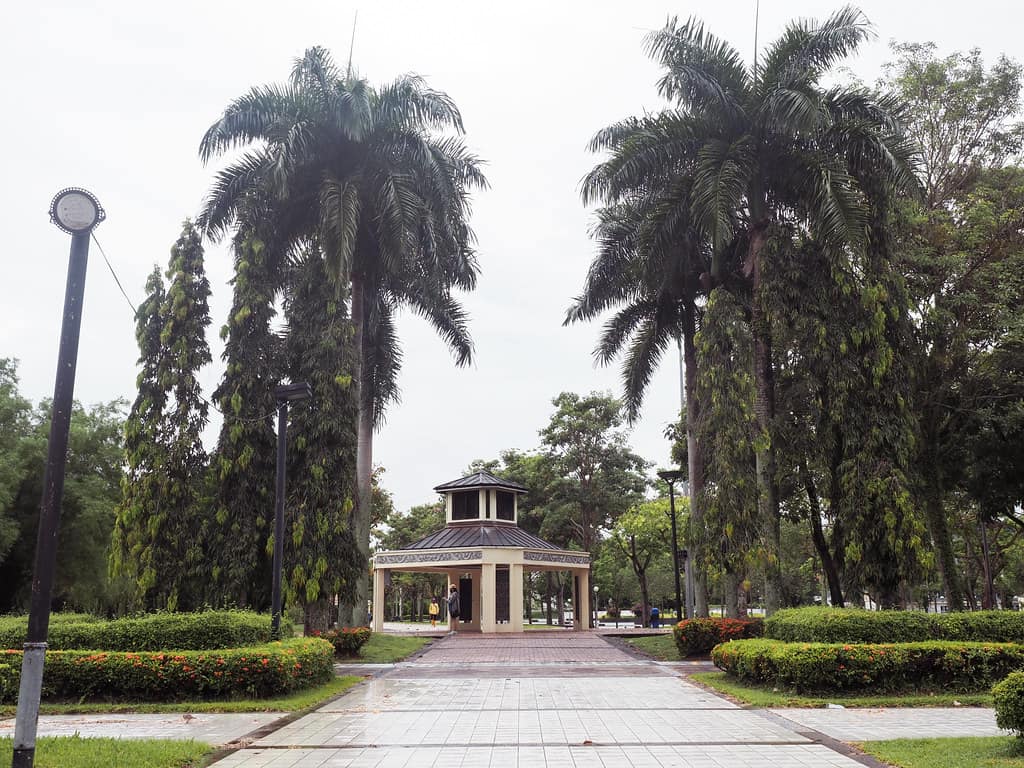A paved avenue between clipped hedges and royal palms leading to the pavilion at Miri City Fan