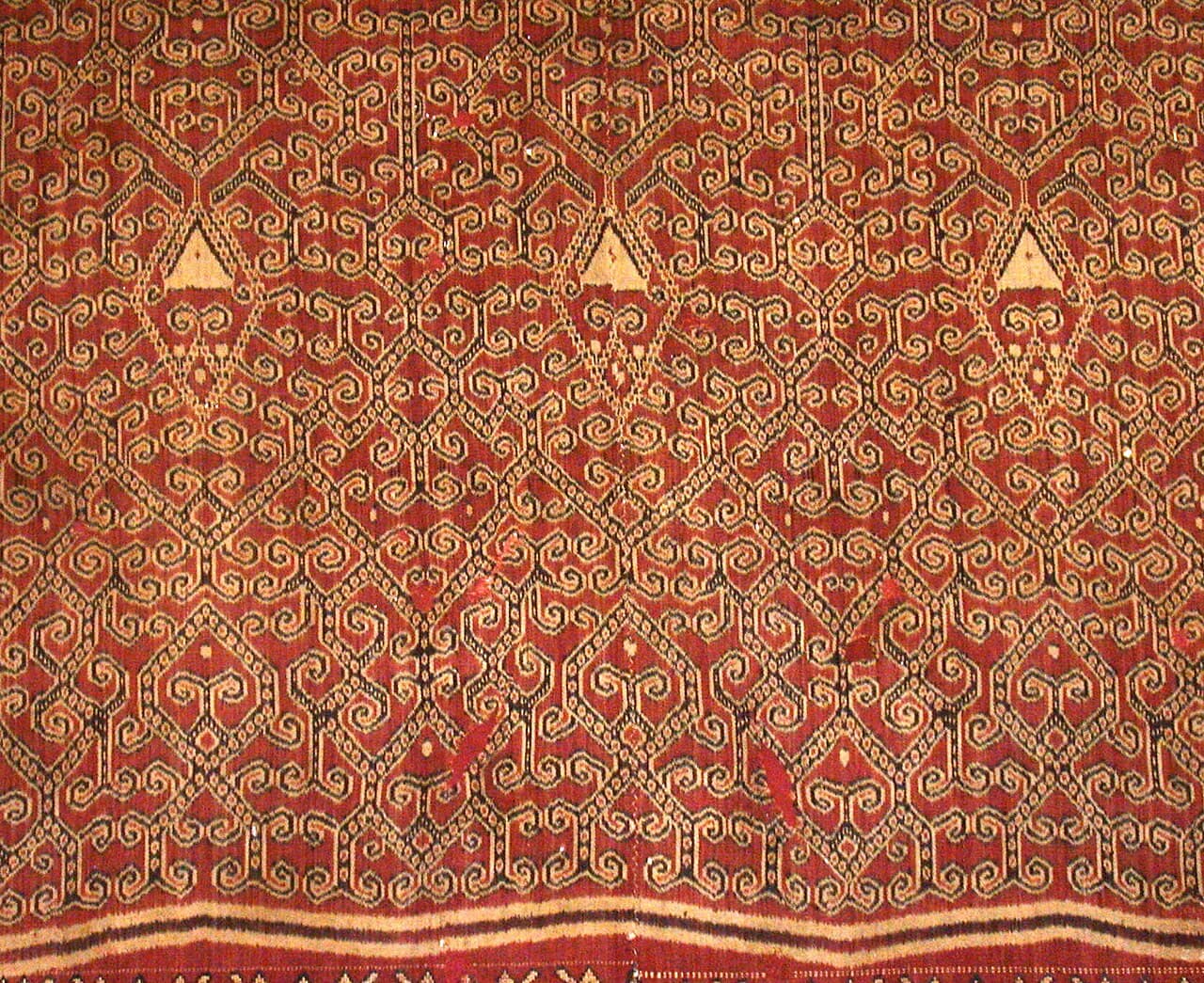 A ceremonial pua kumbu, its rust-red ikat motifs woven in dense repeating bands