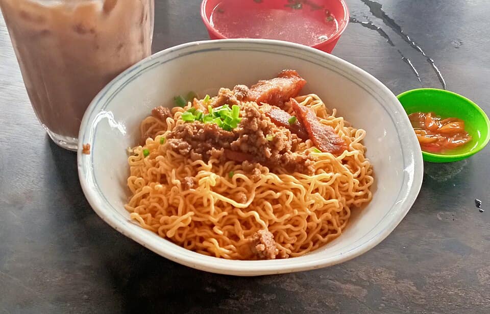 A plate of kolo mee topped with sliced char siu and spring onion