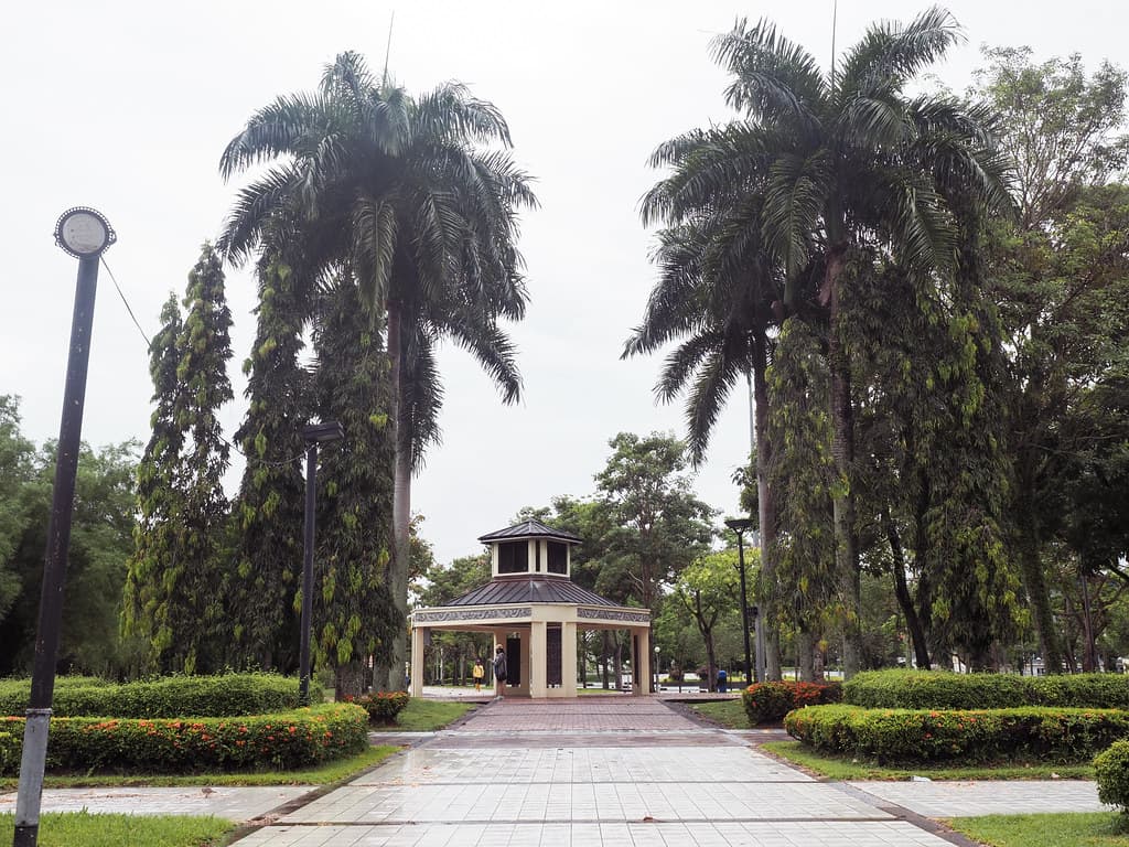A paved avenue between clipped hedges and royal palms leading to the pavilion at Miri City Fan