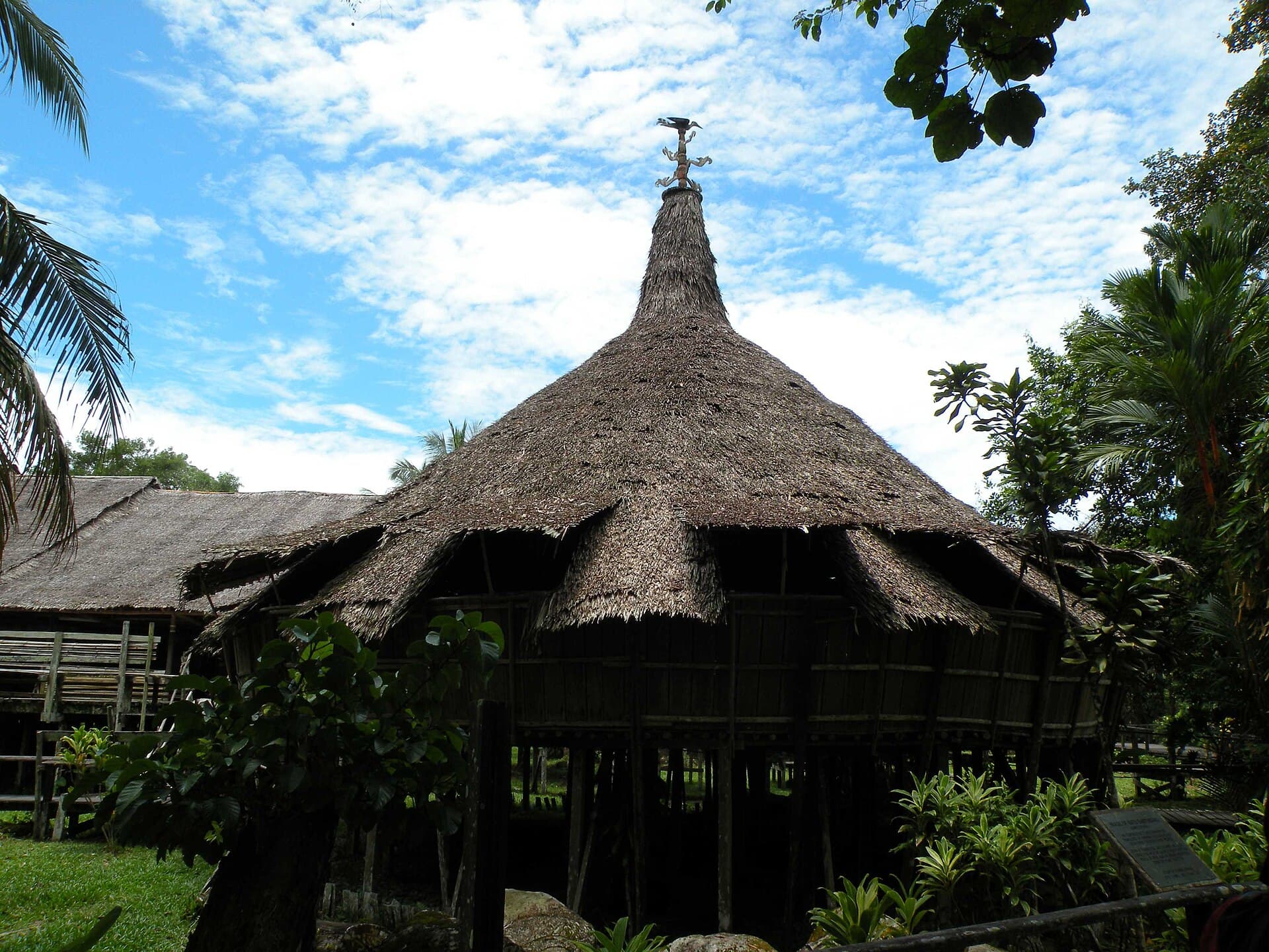 A traditional Bidayuh roundhouse beside lush tropical gardens