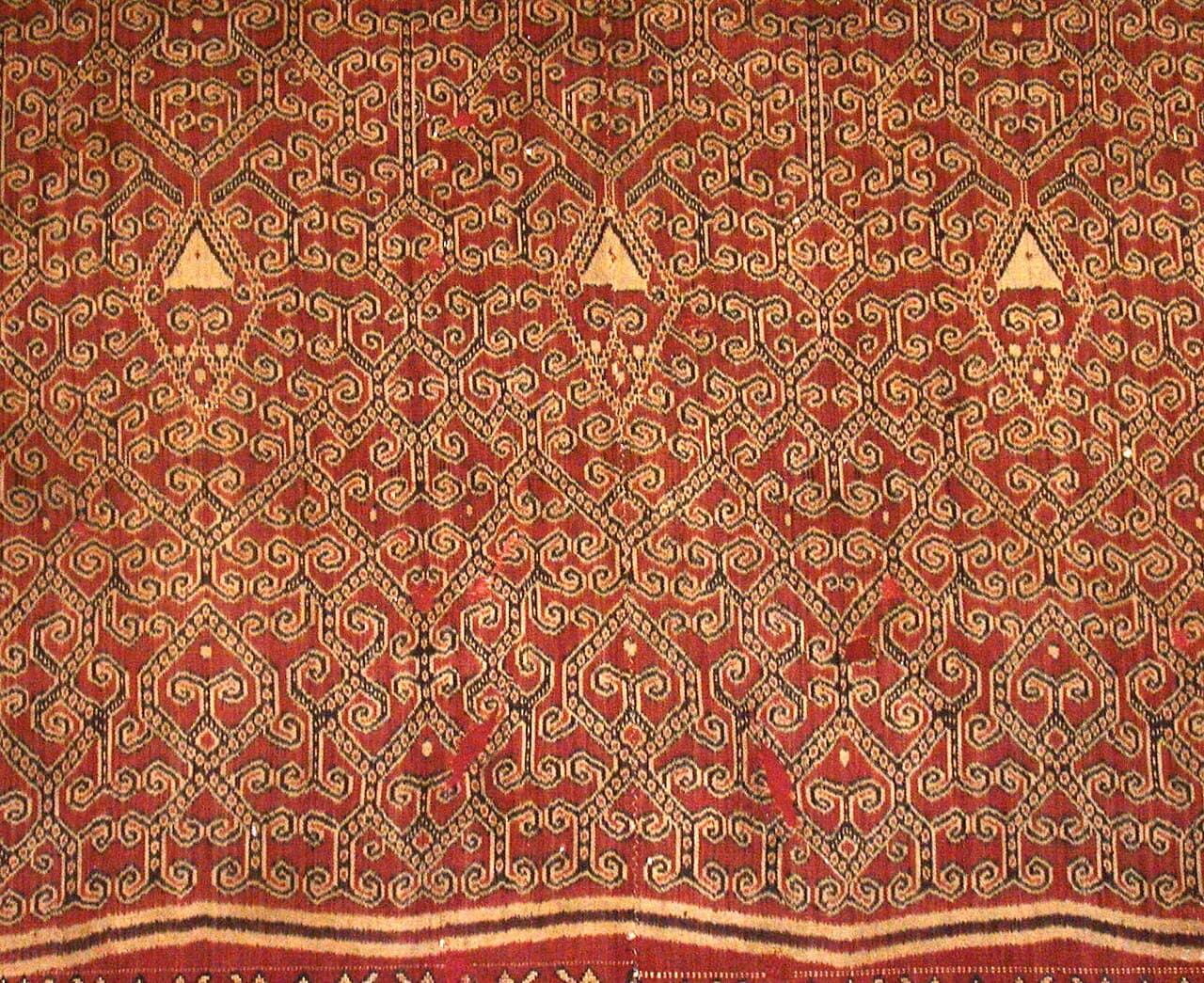 A ceremonial pua kumbu, its rust-red ikat motifs woven in dense repeating bands