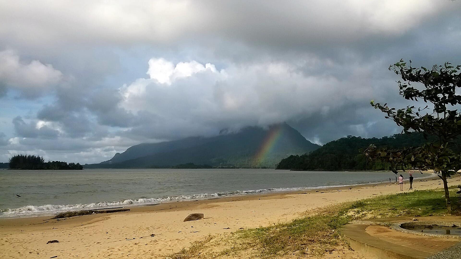 A rainbow over the beach beneath cloud-capped Mount Santubong