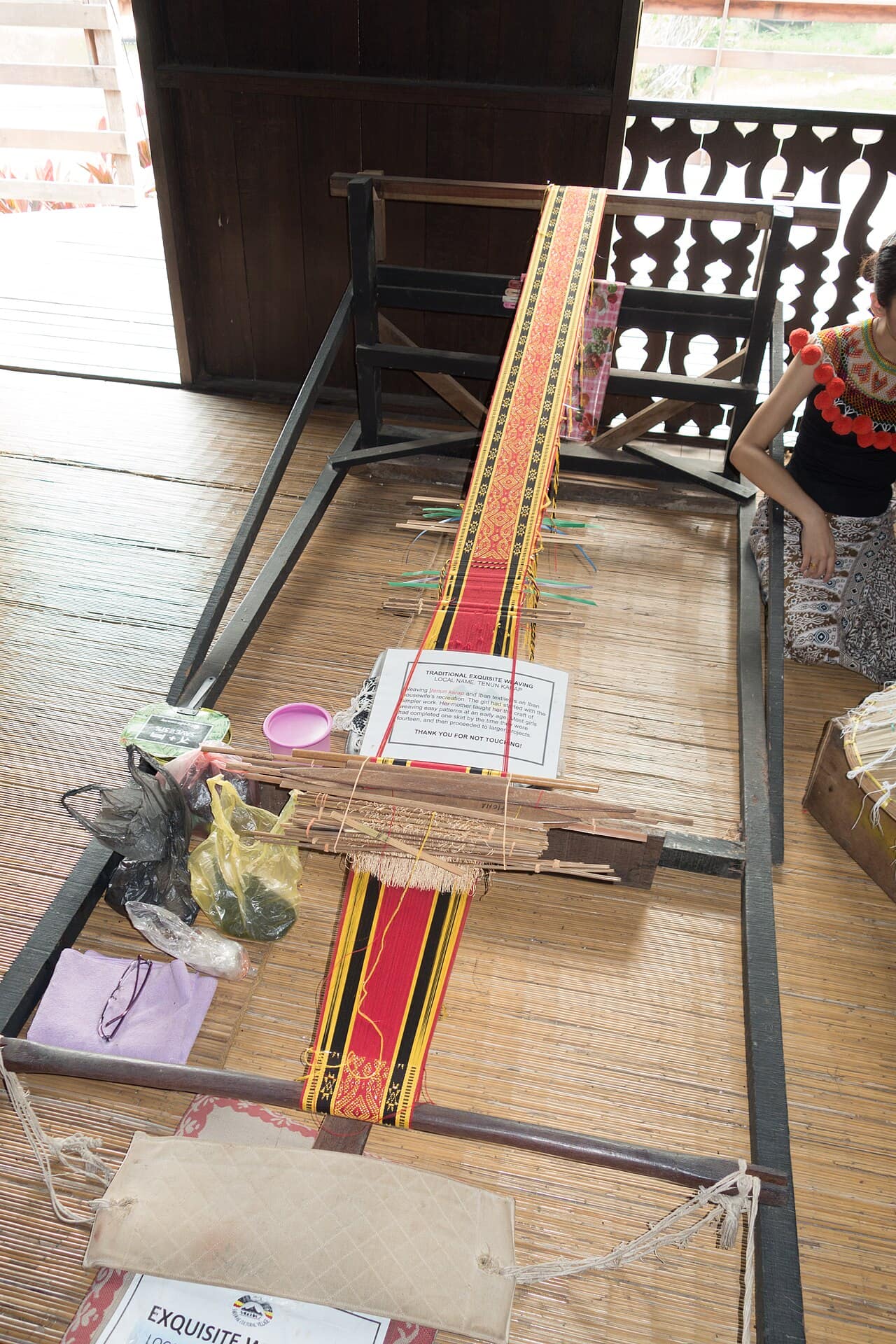 A weaver seated at a backstrap loom working traditional Sarawakian cloth