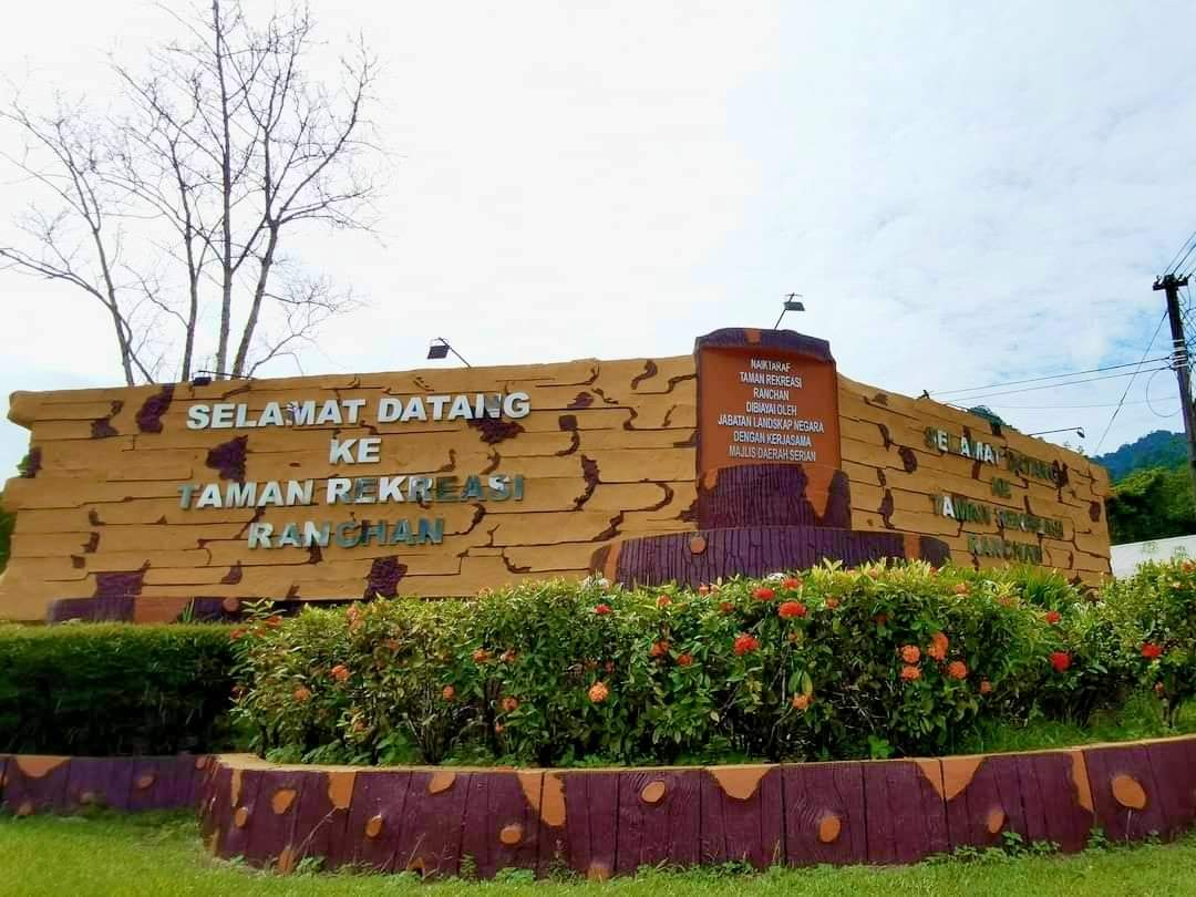 The timber-styled welcome sign reading Selamat Datang ke Taman Rekreasi Ranchan above flowering shrubs