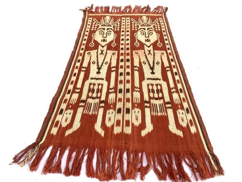 A pua kumbu cloth spread flat, its rust and ecru ikat motifs in repeating bands