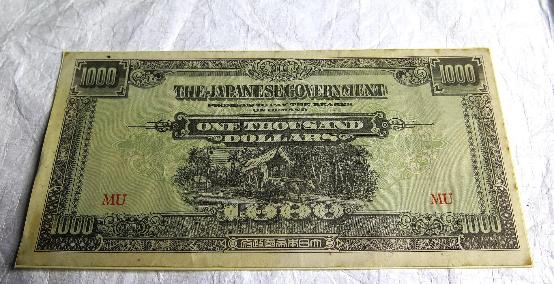 Japanese occupation money Malaya one thousand dollars banknote; marked MU; green and black obverse- 1000 - THE JAPANESE GOVERNMENT - PROMISES TO PAY THE BEARER - ON DEMAND - ONE THOUSAND - DOLLARS - MU - 1000; illustration at centre of buffalo-drawn cart reverse- illustration at centre- villager wit