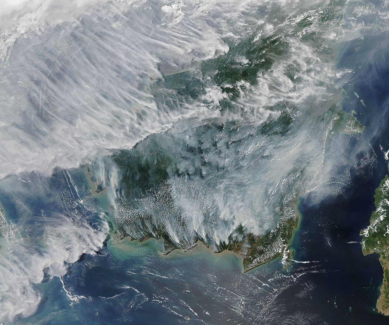 Satellite view of Borneo almost entirely obscured by grey smoke, with fire hotspots burning across Kalimantan